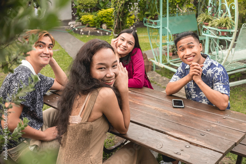 Four friends sitting on a bench at the front yard posing for the camera. Happy and upbeat scene. photo