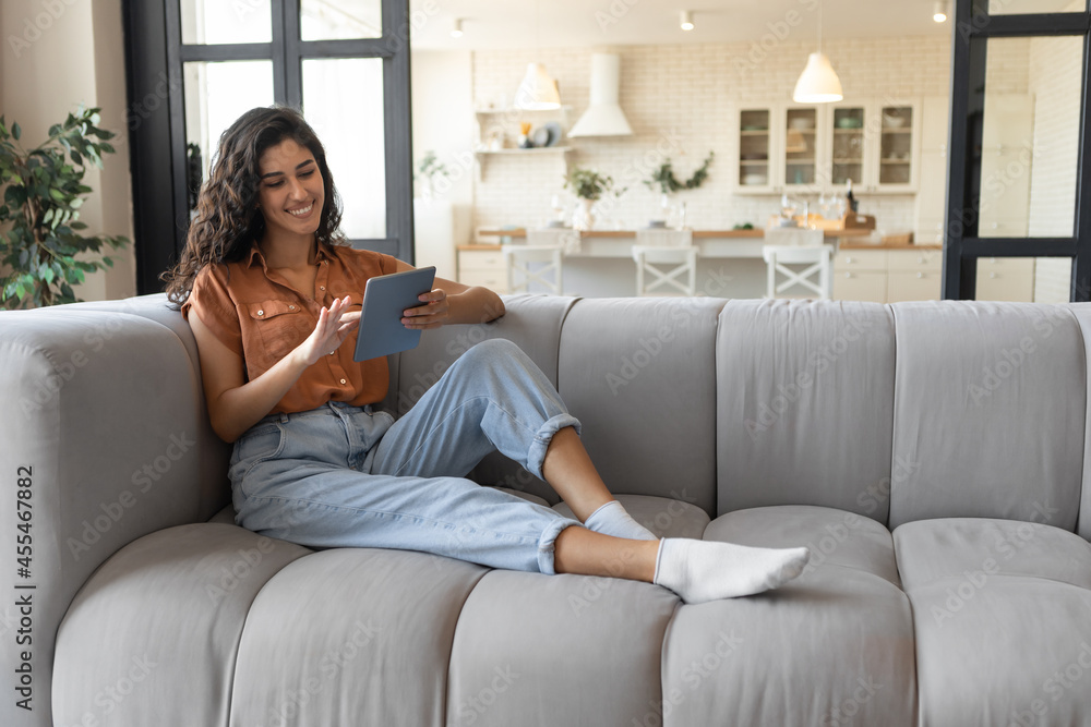 Millennial lady using tablet pc, studying or working remotely, having online conference, sitting on couch at home Millennial lady using tablet pc, studying or working remotely, having online conference, sitting on couch at home