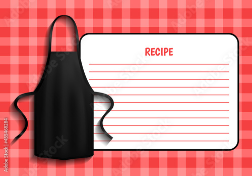 Black apron next to piece of paper with recipe. Clothes for work in kitchen, protective element of clothing for cooking. Apron for cooking in kitchen and protection of clothes near recipe of dish