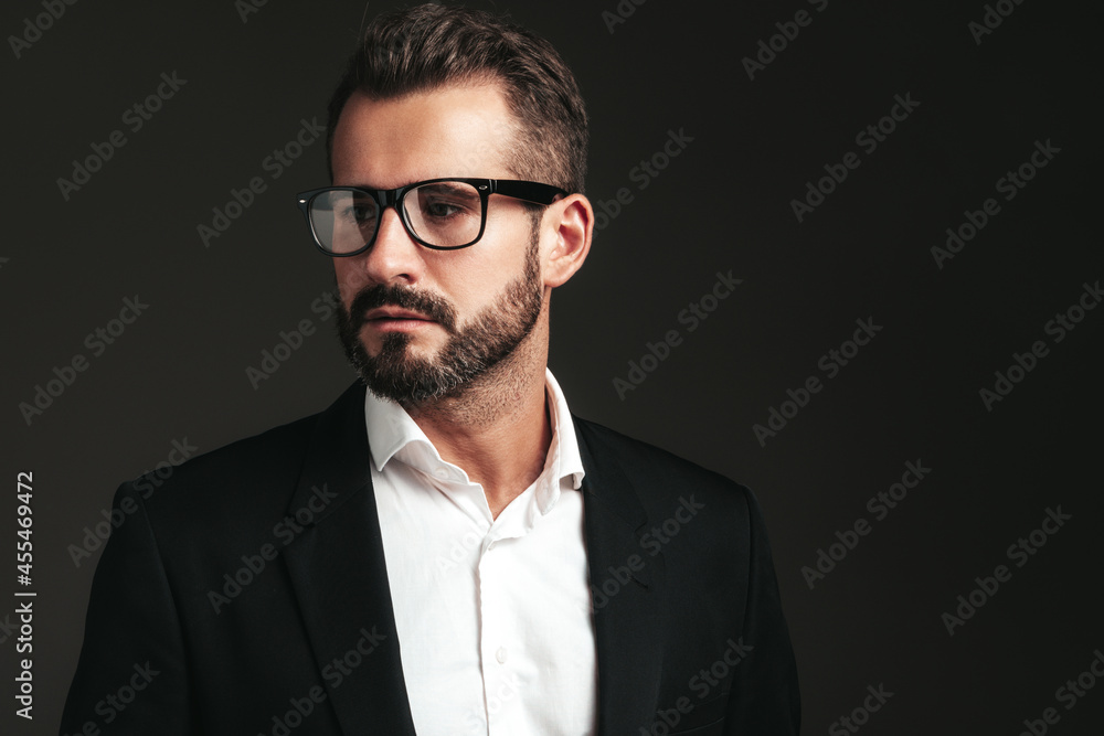 Closeup portrait of handsome confident stylish hipster lambersexual model. Sexy modern man dressed in elegant black suit. Fashion male posing in studio on dark background. In spectacles Closeup portrait of handsome confident stylish hipster lambersexual model. Sexy modern man dressed in elegant black suit. Fashion male posing in studio on dark background. In spectacles