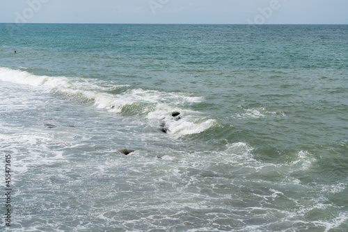 The sea wave foams at the edge of the coast in the rays of sunlight  exposing the coastal stones  in the distance you can see the head of a bathing man