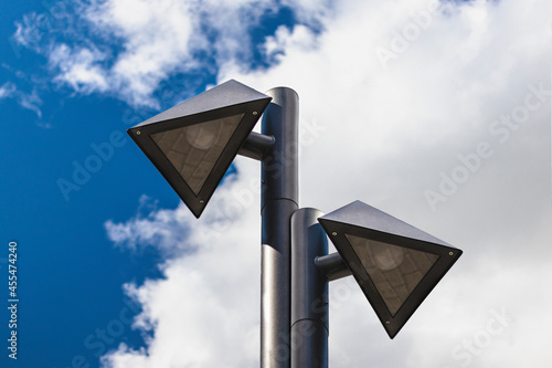 Lamp posts of a triangular shape against a blue cloudy sky. Urban architecture.