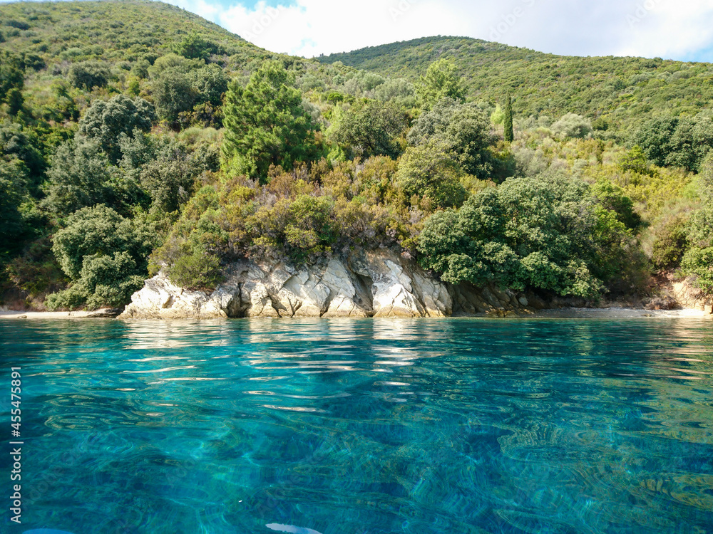 Turquoise clear calm Ionian Sea water with rocky wooded coast and wild nature of Lefkada island in Greece. Summer vacation idyllic travel destination