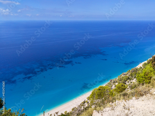 Green cliffs on sunny sea shore on a bright clear blue day in Greece. Turquoise water of Egremni Beach and clear blue sky, Lefkada island, Ionian sea coast photo