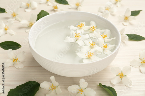 Bowl with water and beautiful jasmine flowers on white wooden table