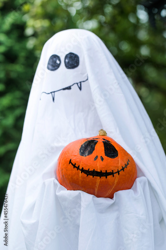 Ghost holds pumpkin with spooky face in green backyard © Виктория Попова
