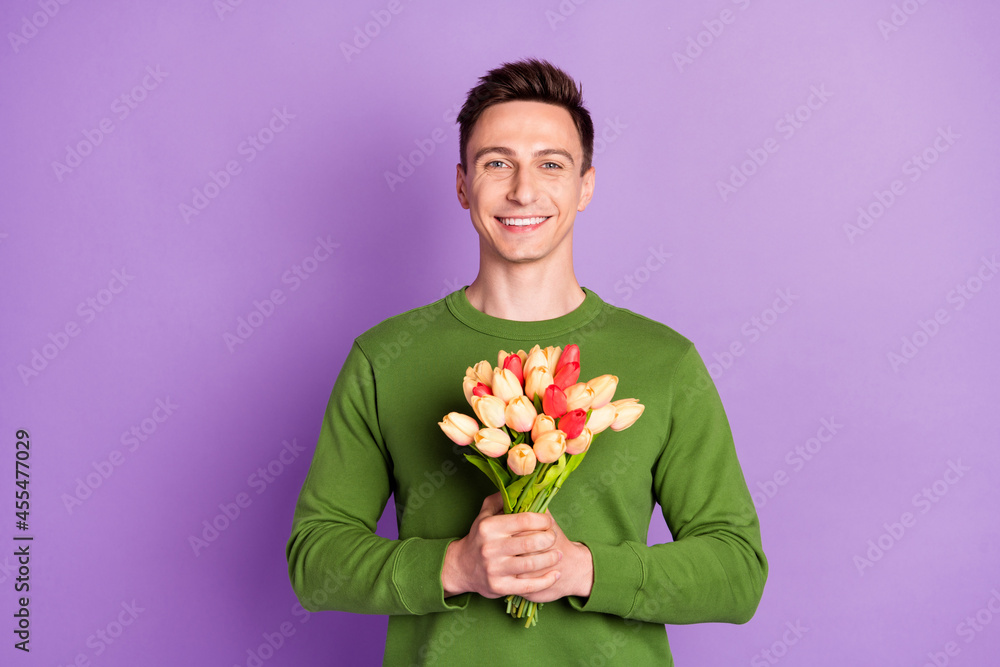 Photo of millennial nice brunet guy hold flowers wear sweater isolated on purple background Photo of millennial nice brunet guy hold flowers wear sweater isolated on purple background