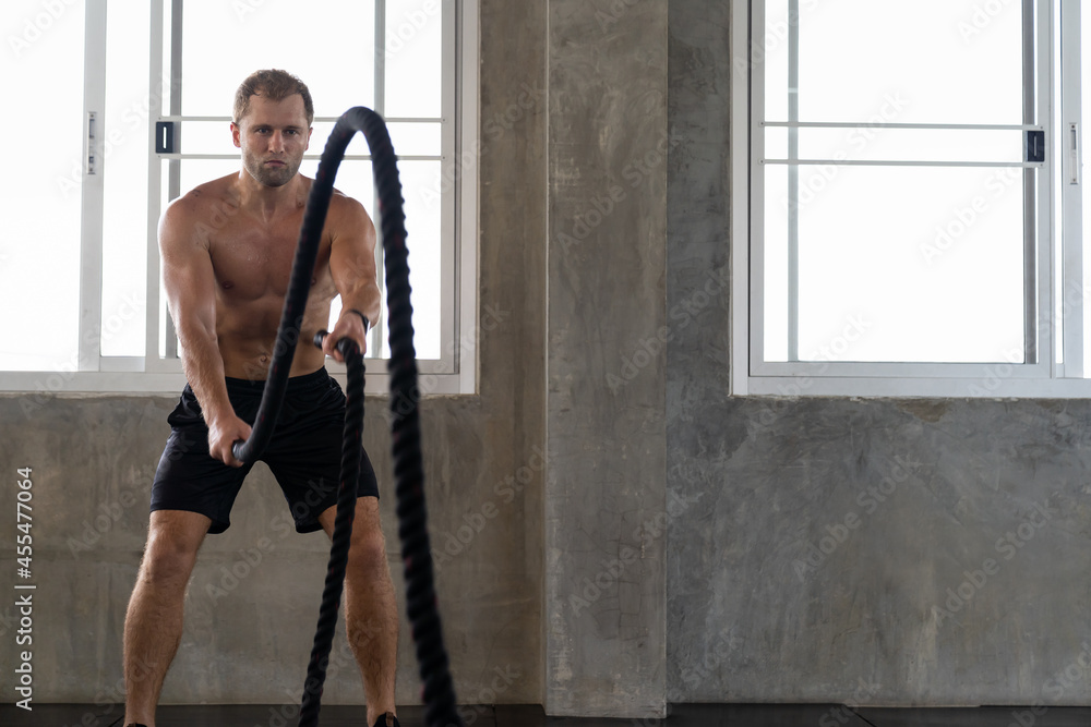 Muscular man doing with battle rope exercise in the sport gym. gym, sport, rope, workout and exercises concept