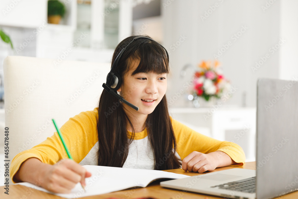Asian girl sitting at table and using laptop during online lessons Asian girl sitting at table and using laptop during online lessons