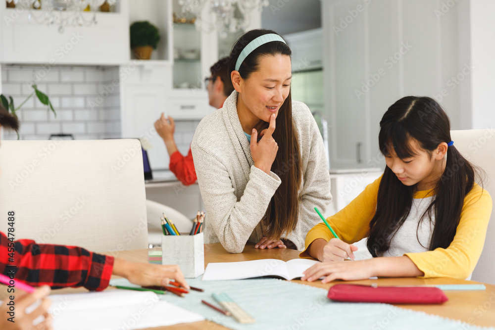 Asian mother helping daughter with school work, with brother in foreground and father in background Asian mother helping daughter with school work, with brother in foreground and father in background