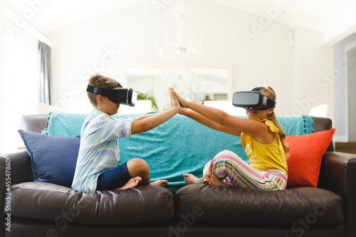 Caucasian brother and sister sitting on couch and using vr headsets in living room