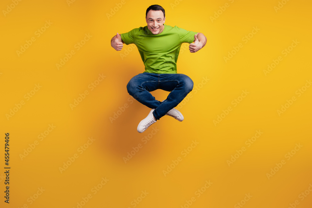 Portrait of funky positive guy jump sport concept raise thumbs up on yellow wall Portrait of funky positive guy jump sport concept raise thumbs up on yellow wall