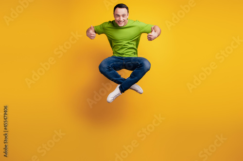 Portrait of funky positive guy jump sport concept raise thumbs up on yellow wall