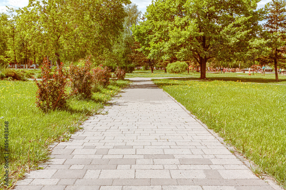 The walkway in the public park is paved with concrete paving slabs of various sizes. Bright illumination by midday sun. The walkway in the public park is paved with concrete paving slabs of various sizes. Bright illumination by midday sun.