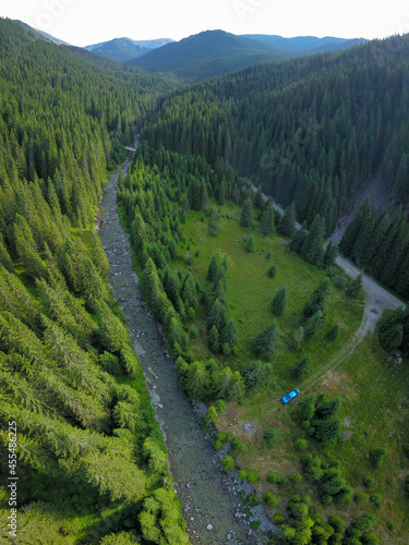 Aerial drone top view above a camping place located in a green meadow near a Loru river. Sunset time. Parang Mountains, Carpathia, Romania.
