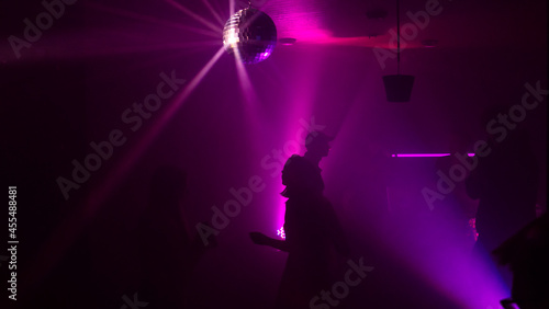 Silhouette image of people dance in disco night club to music from DJ on stage. Party atmosphere with disco ball. Nightlife concept. Space for text. © kalyanby