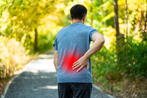 Foto Back pain when walking outdoors, man with kidney inflammation on nature backgrou