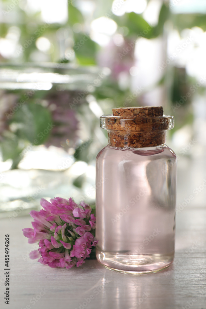 Beautiful clover flower and bottle of essential oil on white wooden table Beautiful clover flower and bottle of essential oil on white wooden table