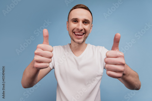 Portrait of excited handsome guy show two arms thumbs up like cool smile isolated on blue color background © Tetiana