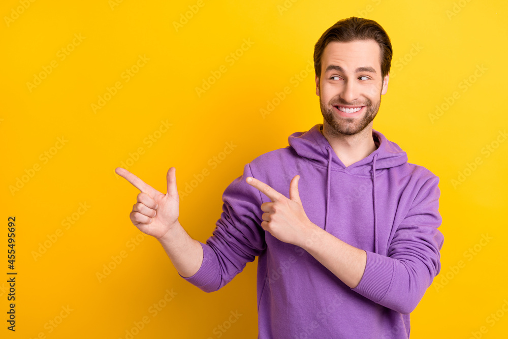 Photo of curious guy direct forefinger empty space look side tips wear violet hoodie isolated yellow color background Photo of curious guy direct forefinger empty space look side tips wear violet hoodie isolated yellow color background