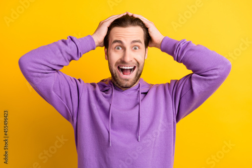 Photo of funky positive astonished guy hands head open mouth wear violet hoodie isolated yellow color background