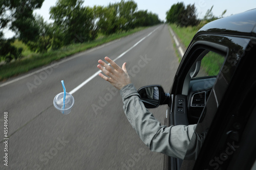 Driver throwing away plastic cup from car window. Garbage on road photo