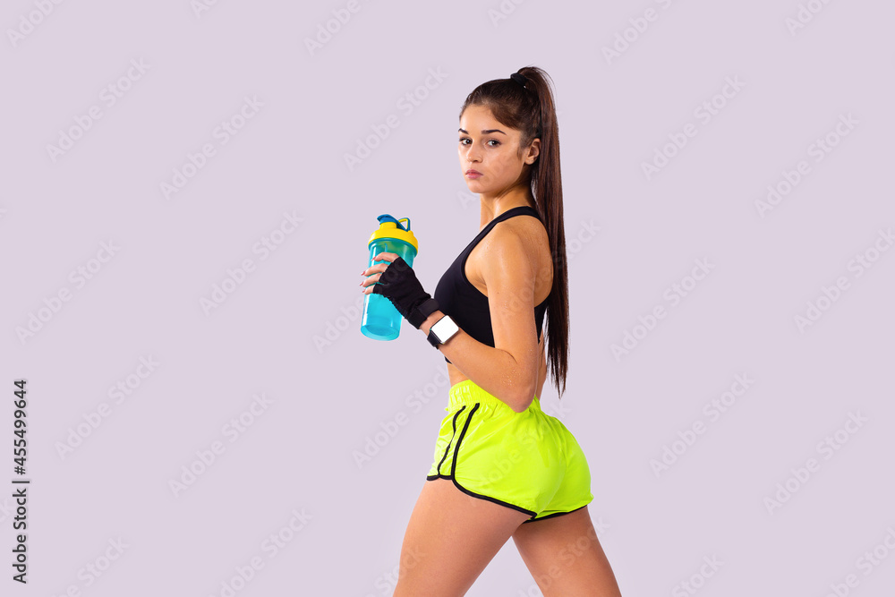 A profile photo of athletic pretty young girl in sportswear holds a jar of protein in her hand over the grey background. A profile photo of athletic pretty young girl in sportswear holds a jar of protein in her hand over the grey background.
