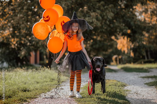 Girl with halloween balloons posing on the street with Labrador retriever.