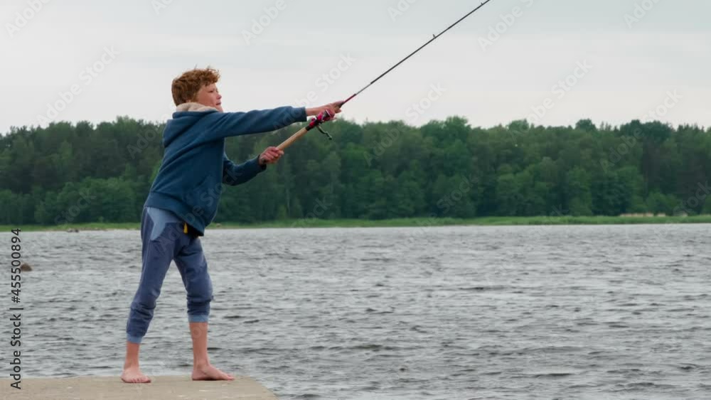 Red-haired Boy on Summer Fishing. Curly red-haired boy throws spinner using spinning on the background of the lake and forest on the horizon Red-haired Boy on Summer Fishing. Curly red-haired boy throws spinner using spinning on the background of the lake and forest on the horizon