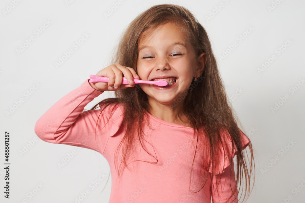Little child girl brushing her teeth on white background.