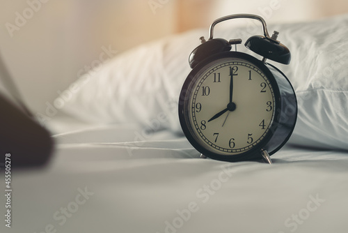 Black vintage alarm clock on white bed in the morning. The hands of the clock pointing to eight o'clock. but set an alarm for seven o'clock in the morning.