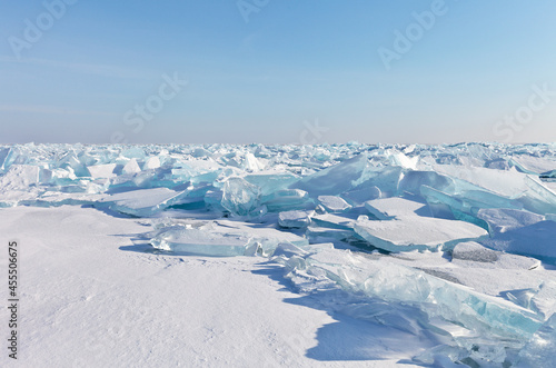 Beautiful winter landscape of frozen Lake Baikal. Endless snow-covered field with transparent blue ice floes on ice hummocks on a frosty sunny day. Natural cold background. Empty space for text