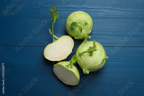 Whole and cut kohlrabi plants on blue wooden table, flat lay