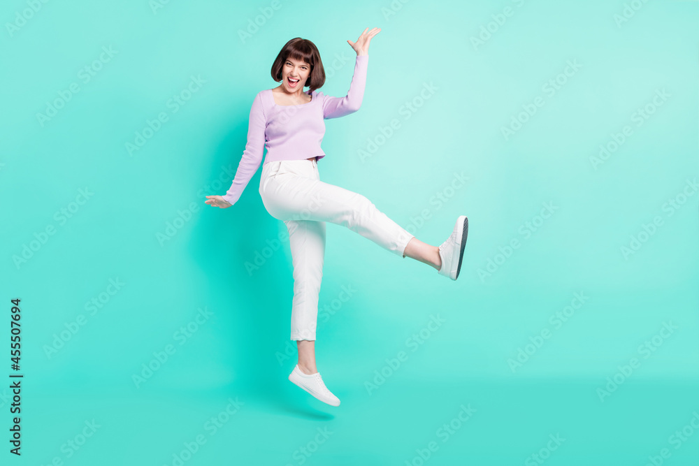 Full length photo of cute adorable young lady wear purple pullover walking jumping high smiling isolated teal color background Full length photo of cute adorable young lady wear purple pullover walking jumping high smiling isolated teal color background