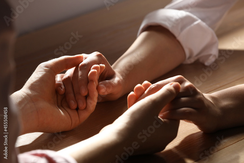 Religious women holding hands and praying together at wooden table, closeup