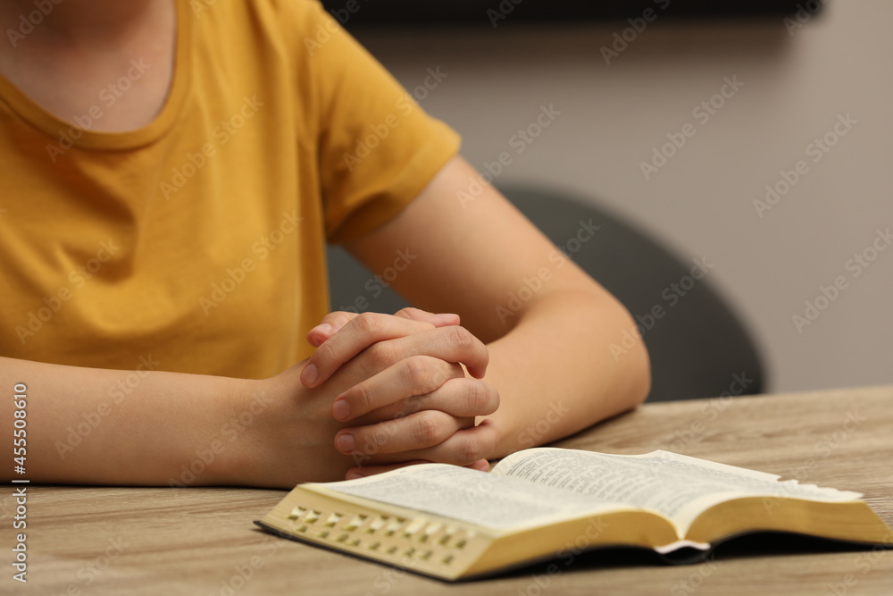 Religious woman praying over Bible at wooden table indoors, closeup Religious woman praying over Bible at wooden table indoors, closeup