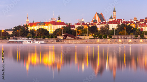 Illuminated Warsaw Old Town panorama with the Royal Castle, Cathedral and medieval buildings, during sunrise with reflections in calm Vistula river, Poland.