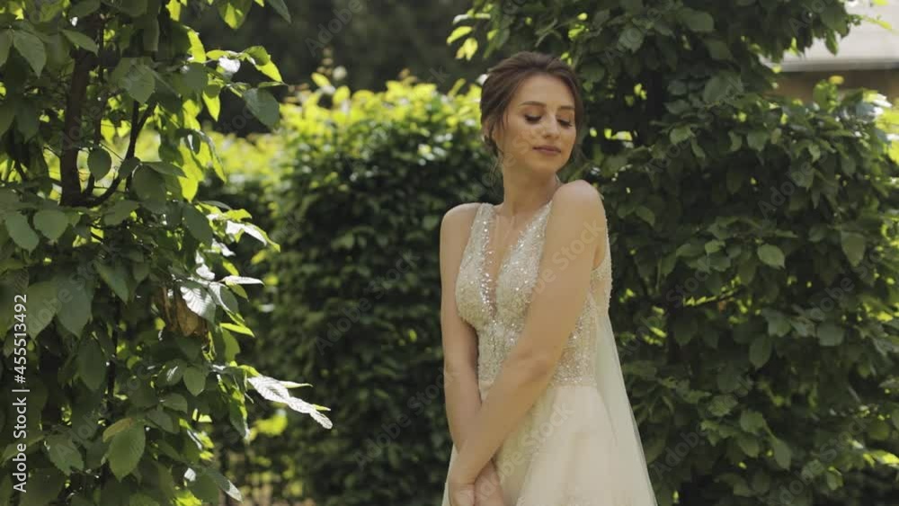 Beautiful lovely stylish bride in white wedding dress and veil in the park waiting for groom. Pretty and well-groomed fashionable woman with fashion hairstyle and makeup. Wedding day. Slow motion Beautiful lovely stylish bride in white wedding dress and veil in the park waiting for groom. Pretty and well-groomed fashionable woman with fashion hairstyle and makeup. Wedding day. Slow motion