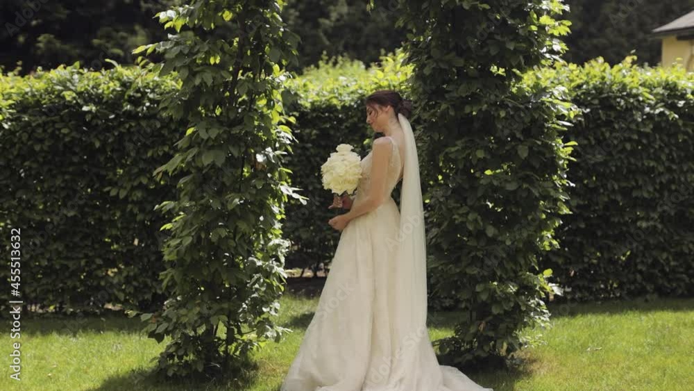 Beautiful lovely stylish bride in white wedding dress and veil holding wedding bouquet in hands in park waiting for groom. Pretty and well-groomed fashionable woman with hairstyle, makeup. Wedding day Beautiful lovely stylish bride in white wedding dress and veil holding wedding bouquet in hands in park waiting for groom. Pretty and well-groomed fashionable woman with hairstyle, makeup. Wedding day