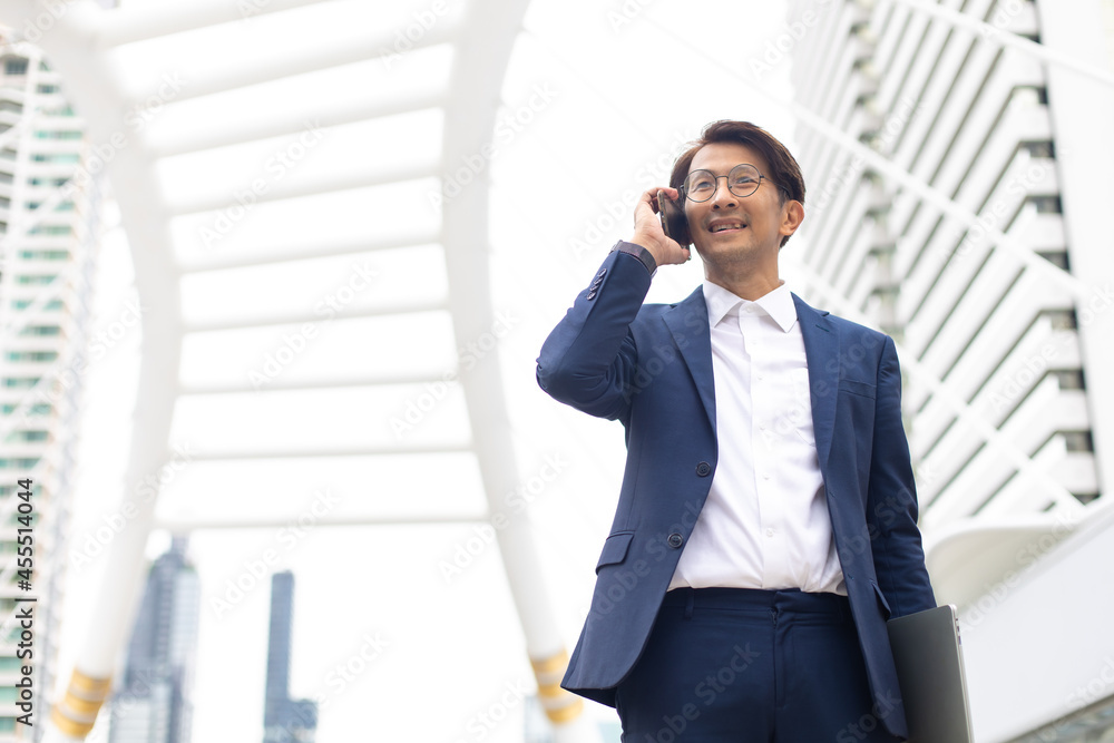 Asian businessman using mobile phone app texting outside the office building Asian businessman using mobile phone app texting outside the office building