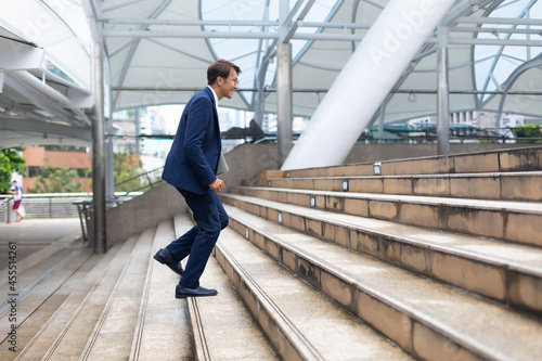 Asian businessman wearing suit jacket running fast upstairs go to work in morning outdoor.