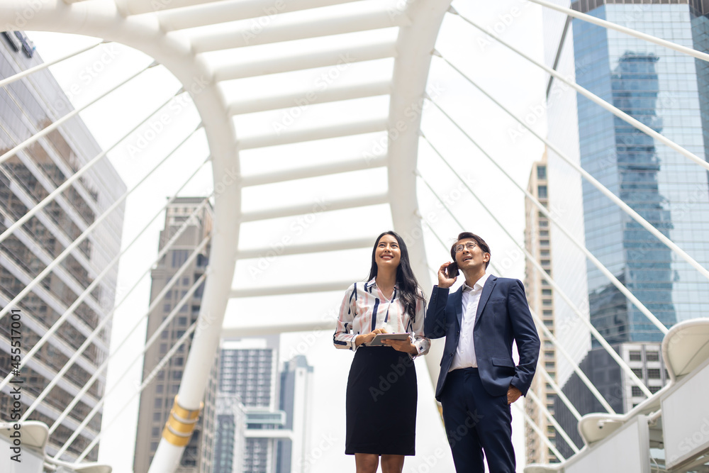 Asian business man talking on mobile phone and young beautiful woman working on digital tablet computer standing outside office building. Asian business man talking on mobile phone and young beautiful woman working on digital tablet computer standing outside office building.