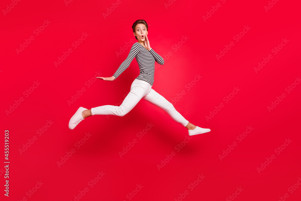 Photo of shiny impressed young woman dressed striped outfit arm cheek jumping hign isolated red color background Photo of shiny impressed young woman dressed striped outfit arm cheek jumping hign isolated red color background