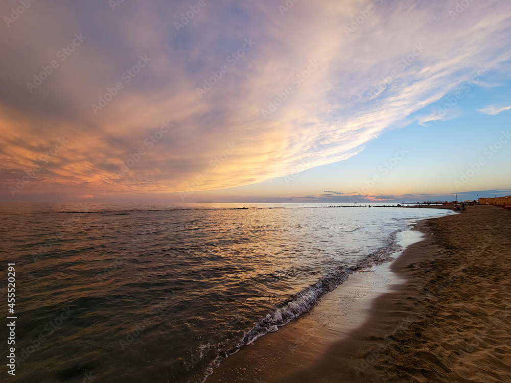 Obraz premium Sunset on the shore of the beach. Multicolored sky, spectacular sunset over the sea with waves on the beach.