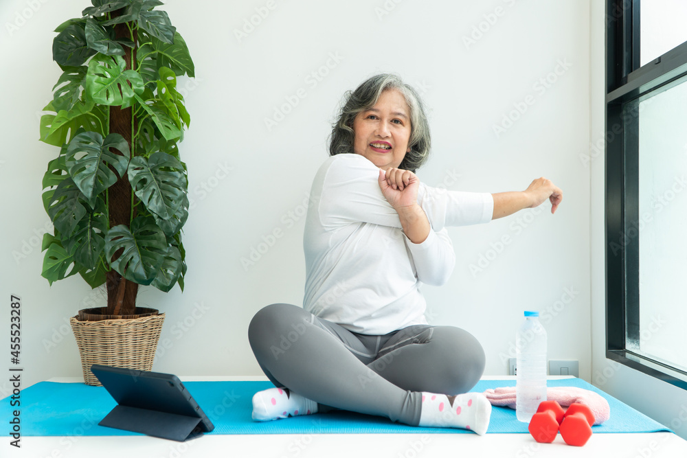 Senior Asian woman watching online courses on a laptop while exercising in the living room at home. Concept of workout training online. Senior Asian woman watching online courses on a laptop while exercising in the living room at home. Concept of workout training online.