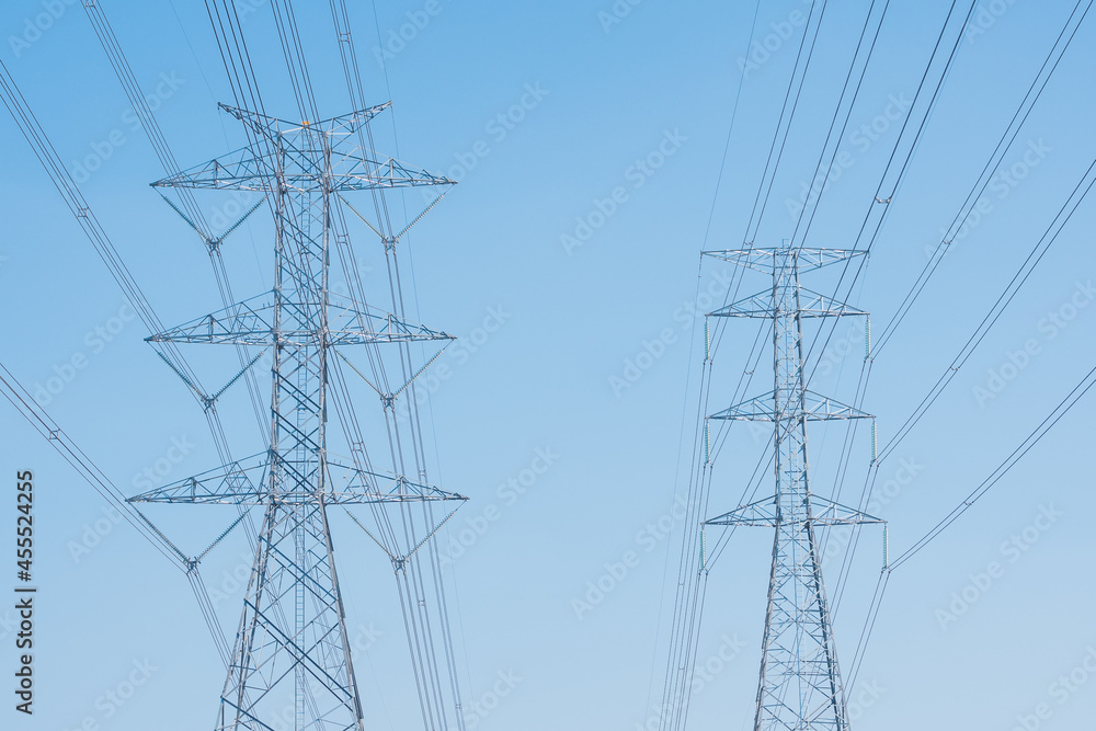 Two High voltage pole stand agianst white clouds and clear blue sky background
