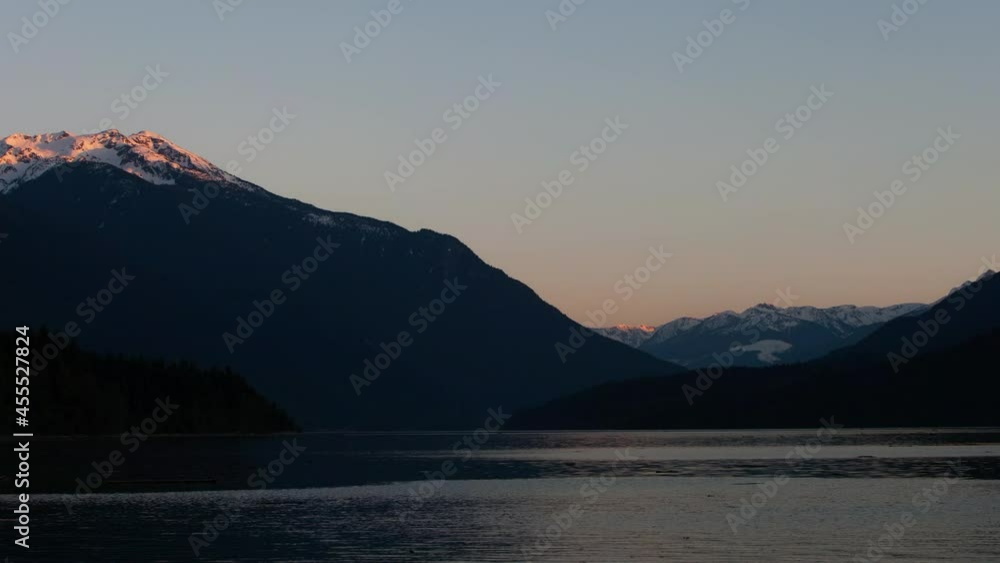 Time Lapse Lockdown Shot Of Beautiful Rocky Mountains Against Clear Sky By Lake During Winter - Vancouver, Canada Time Lapse Lockdown Shot Of Beautiful Rocky Mountains Against Clear Sky By Lake During Winter - Vancouver, Canada