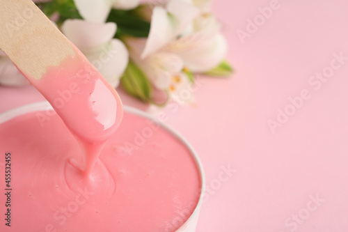 Wooden spatula and hot depilatory wax on light pink background, closeup. Space for text photo