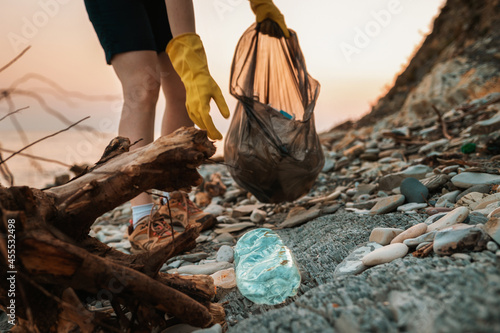 Envinmental pollution. Close up of volunteer\'s hands with plastic bag picks up a dirty bottle. The concept of Earth Day. Low angle
