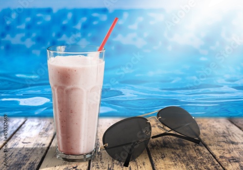 Ice cocktail against blue clear water of the swimming pool, on table, with sunglasses. photo